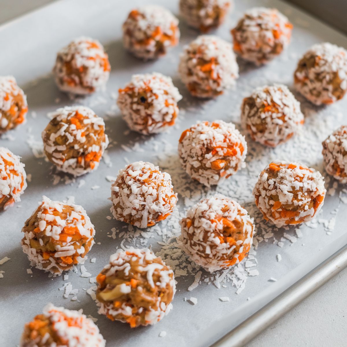 Sticky dough rolled into balls, coated with shredded coconut, and placed on a parchment-lined baking sheet.