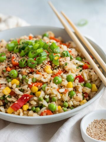 Close-up of cauliflower fried rice with colorful vegetables, sesame seeds, and scallions, served with chopsticks.