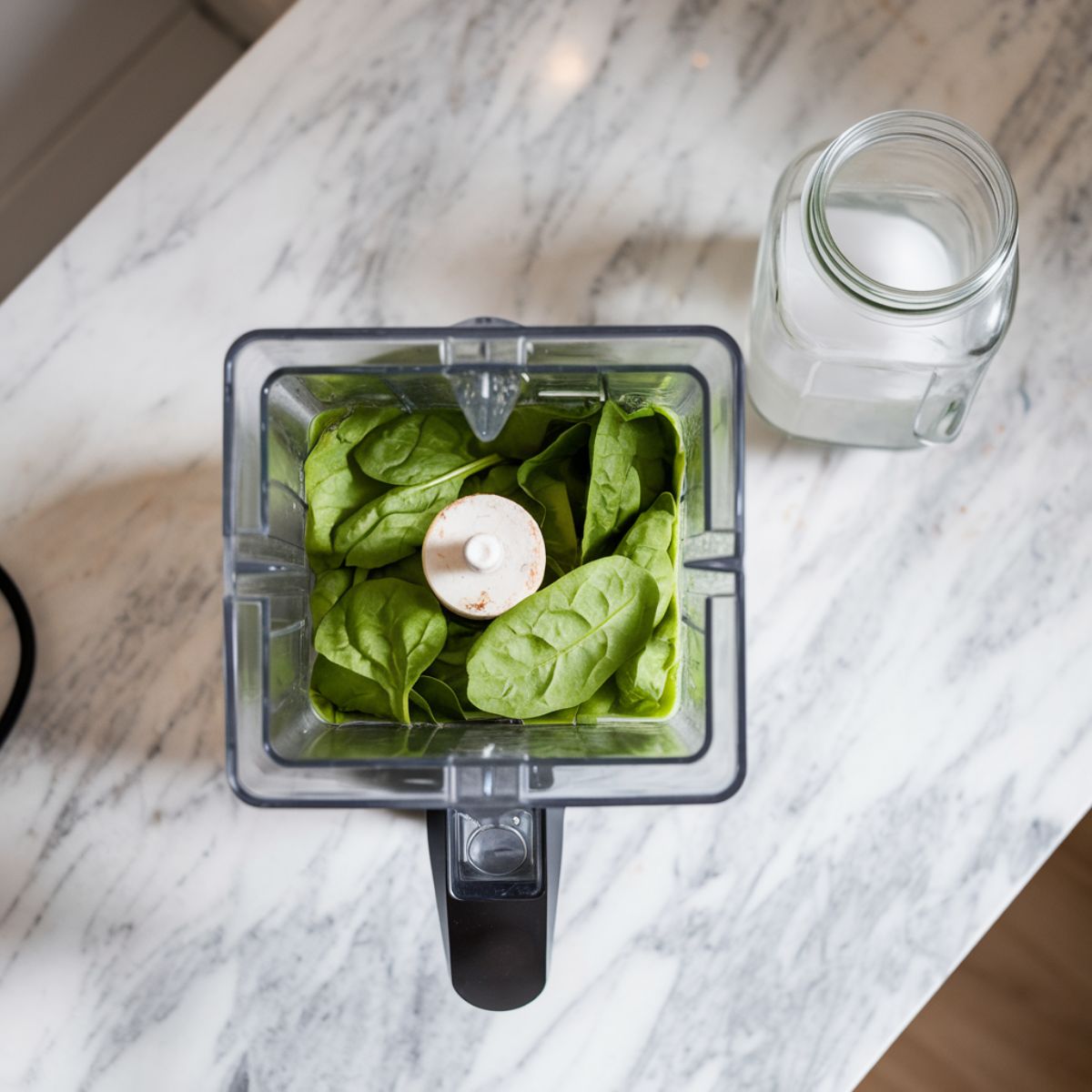 Blender filled with spinach and coconut water mid-blend, creating a vibrant green mixture, with a jug of coconut water nearby.