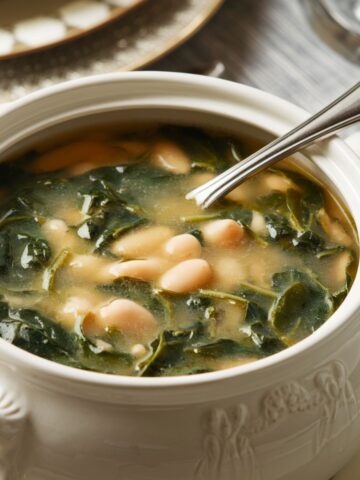 A bowl of spinach and white bean soup with a golden broth and a silver spoon.