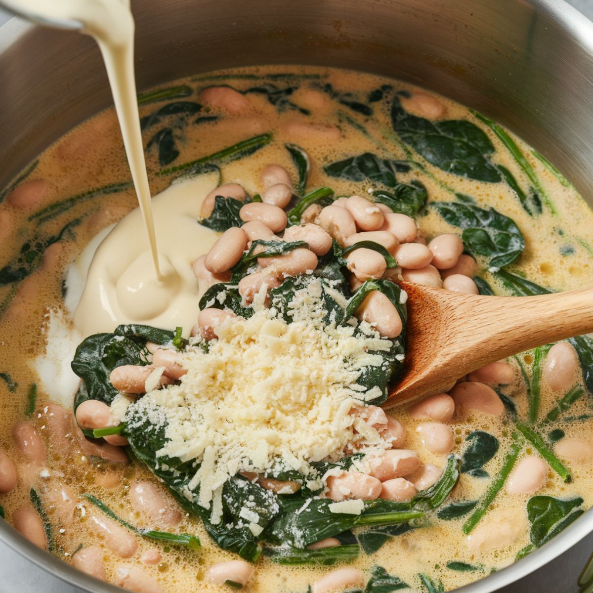 Creamy soup with wilted spinach, cream being poured in, and Parmesan cheese melting on top.