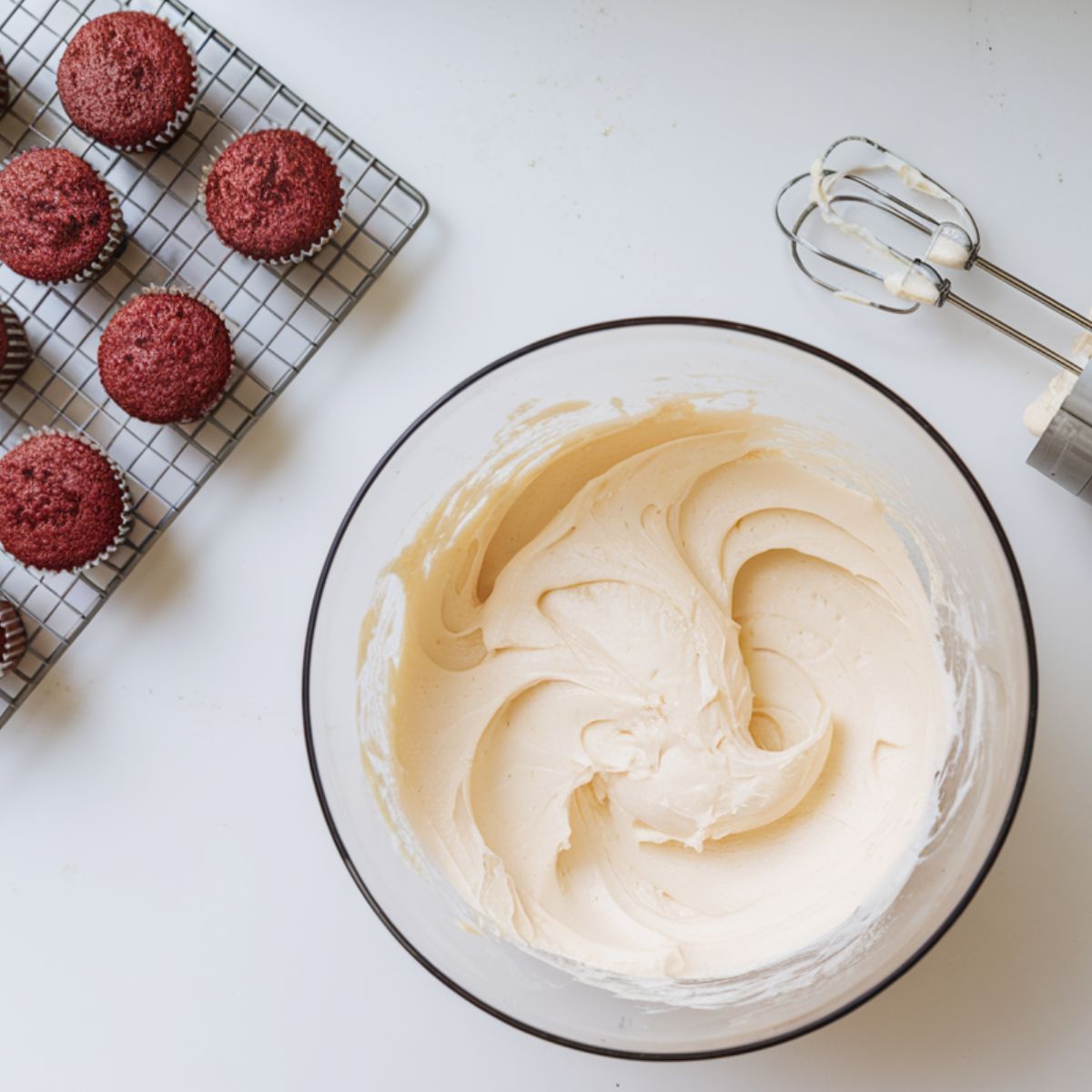 Beating cream cheese and butter with powdered sugar, vanilla extract, and salt in a modern kitchen with a garden view.