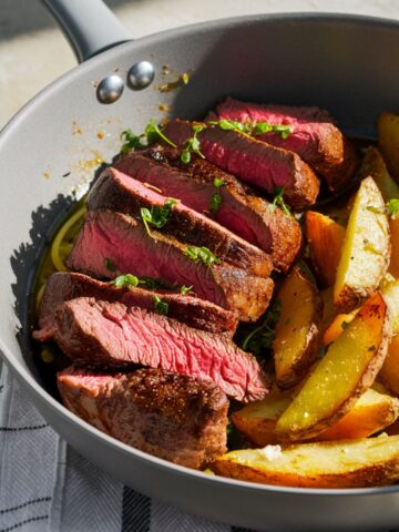 Skillet with sliced medium-rare steak and potatoes , garnished with fresh herbs.