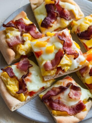 Homemade breakfast pizza bites fresh out of the oven, with crispy edges and gooey melted cheese, served on a plate on a kitchen counter.