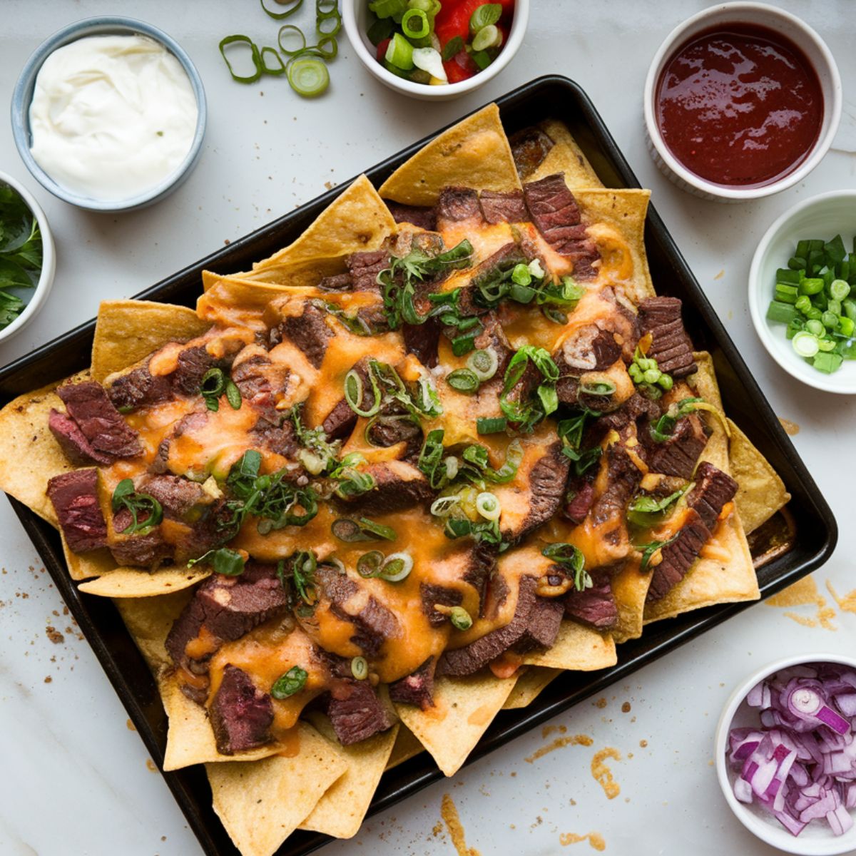 Fresh toppings being added to hot, cheesy nachos on a white marble countertop for steak nachos recipe.