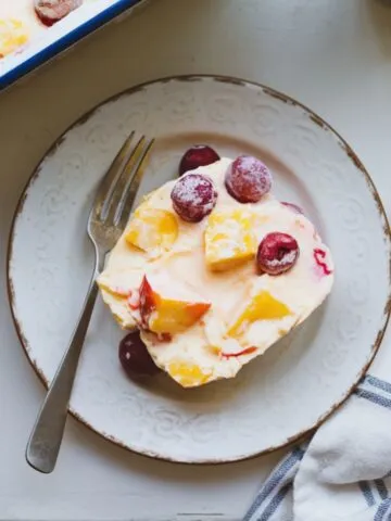 A homemade frozen fruit salad slice on a rustic white plate, showing colorful fruit pieces in a creamy base.