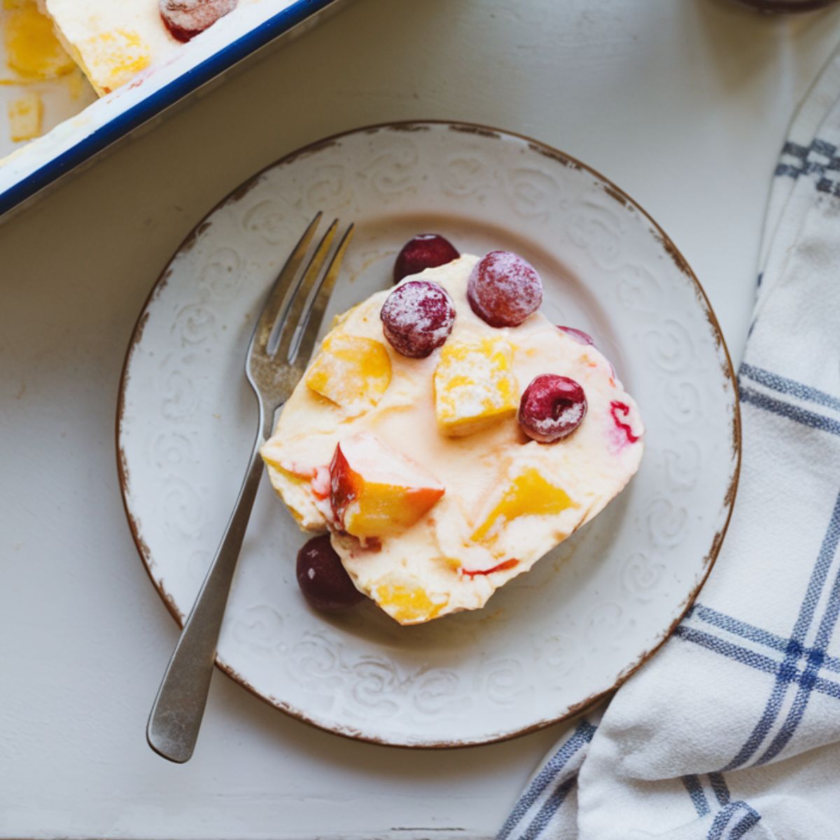  A homemade frozen fruit salad slice on a rustic white plate, showing colorful fruit pieces in a creamy base.