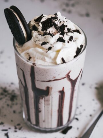 Homemade Oreo milkshake topped with whipped cream and crushed Oreos on a kitchen counter.