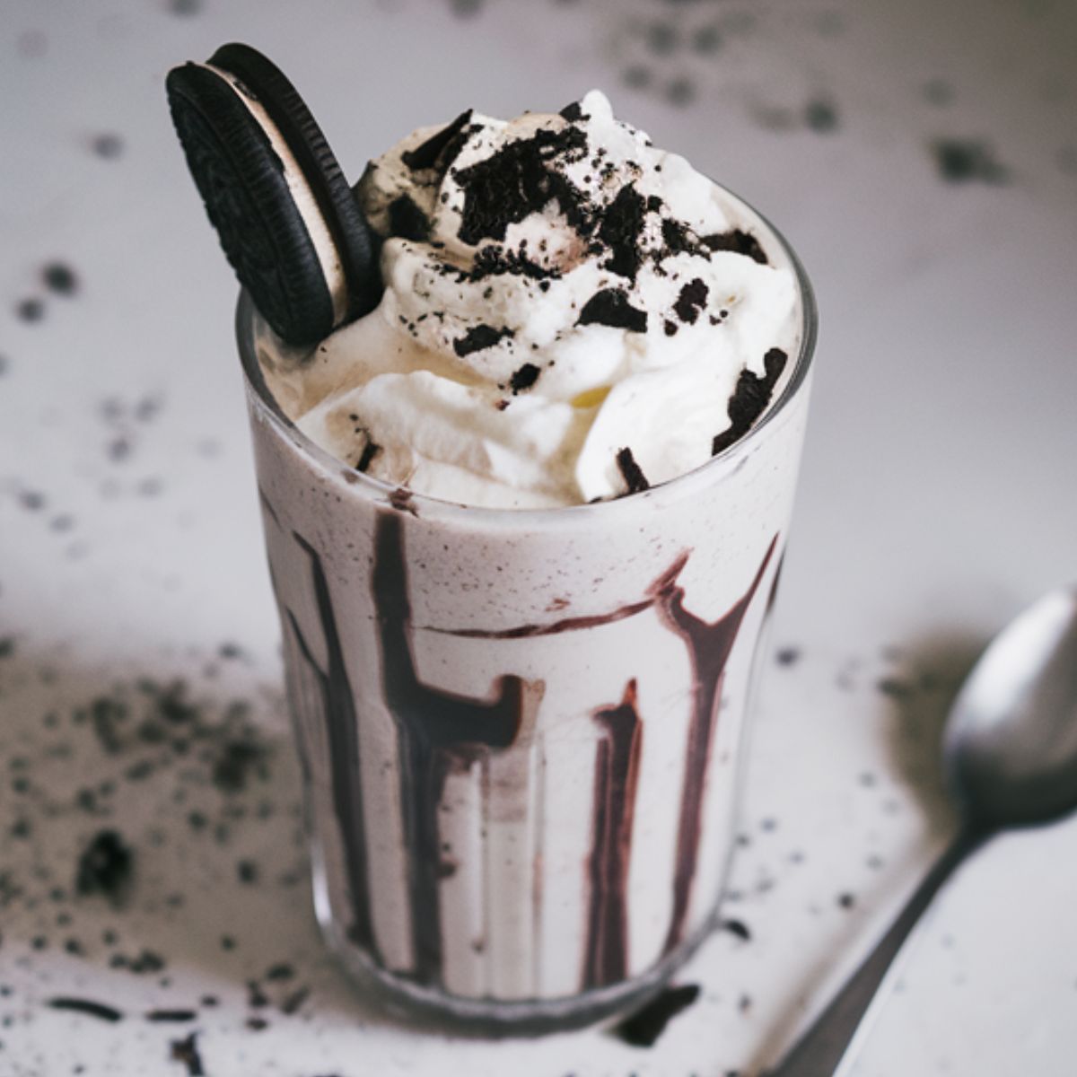 Homemade Oreo milkshake topped with whipped cream and crushed Oreos on a kitchen counter.