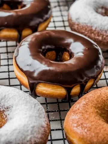 Homemade sourdough donuts with chocolate glaze, powdered sugar, and cinnamon sugar on a cooling rack.