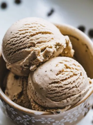 A homemade scoops of coffee ice cream in a rustic bowl with coffee beans scattered around.