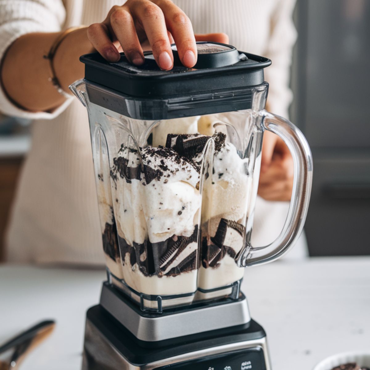 A blender filled with ice cream, milk, and crushed Oreos, ready to blend.