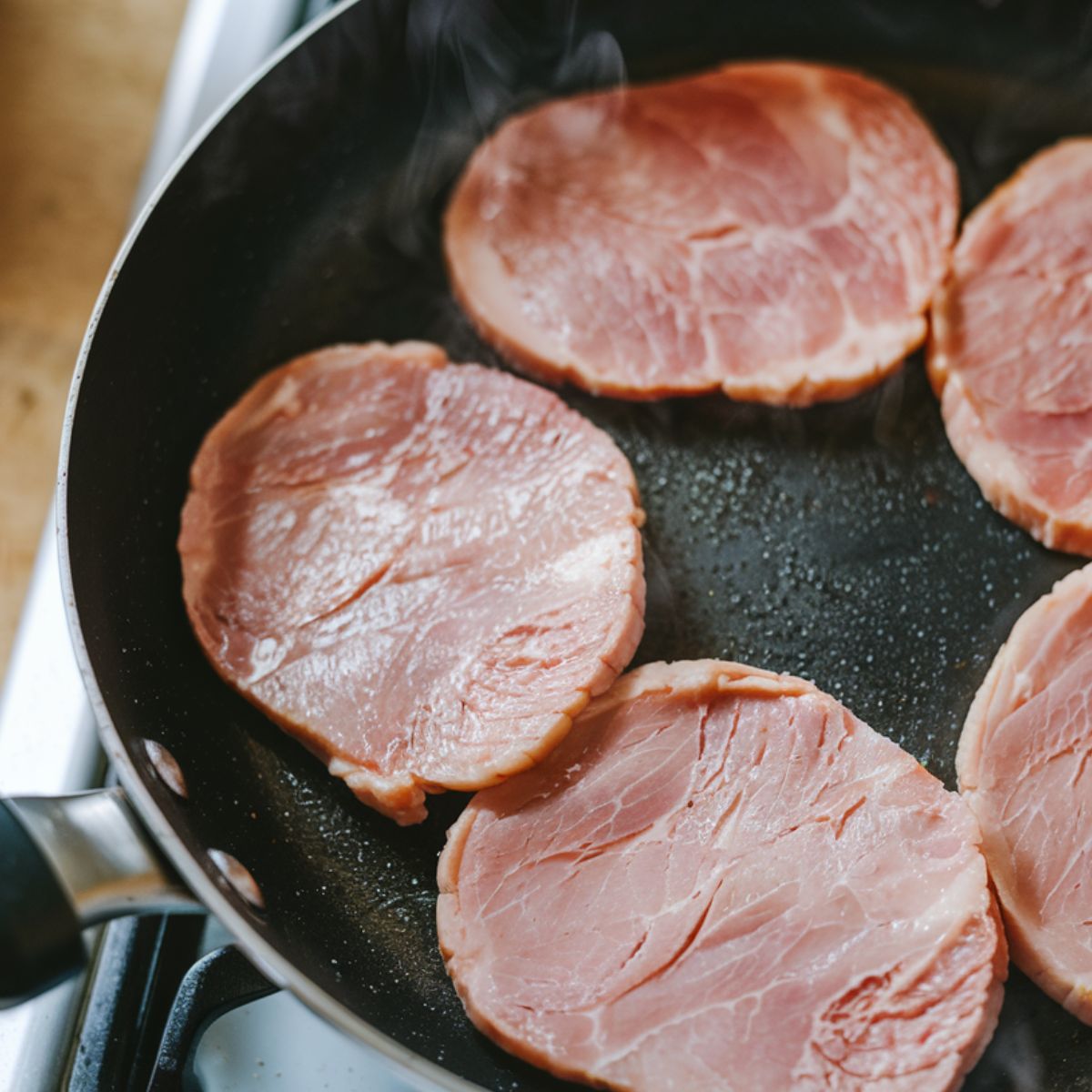 A frying pan with  ham slices cooking.