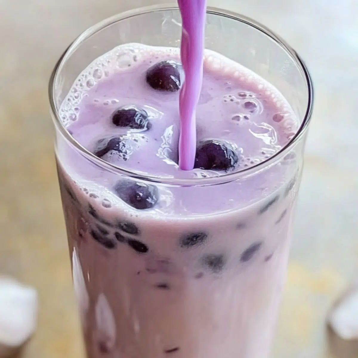 Pouring homemade taro milk tea over tapioca pearls in a tall glass