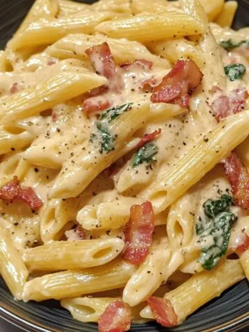 Creamy bacon pasta served in a bowl on a kitchen counter with visible bacon bits and parmesan