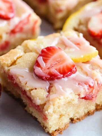 Freshly baked strawberry lemon blondies on a white kitchen counter with glaze and crumbs