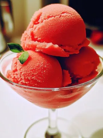 Homemade strawberry sorbet in a bowl with fresh mint on a white kitchen counter