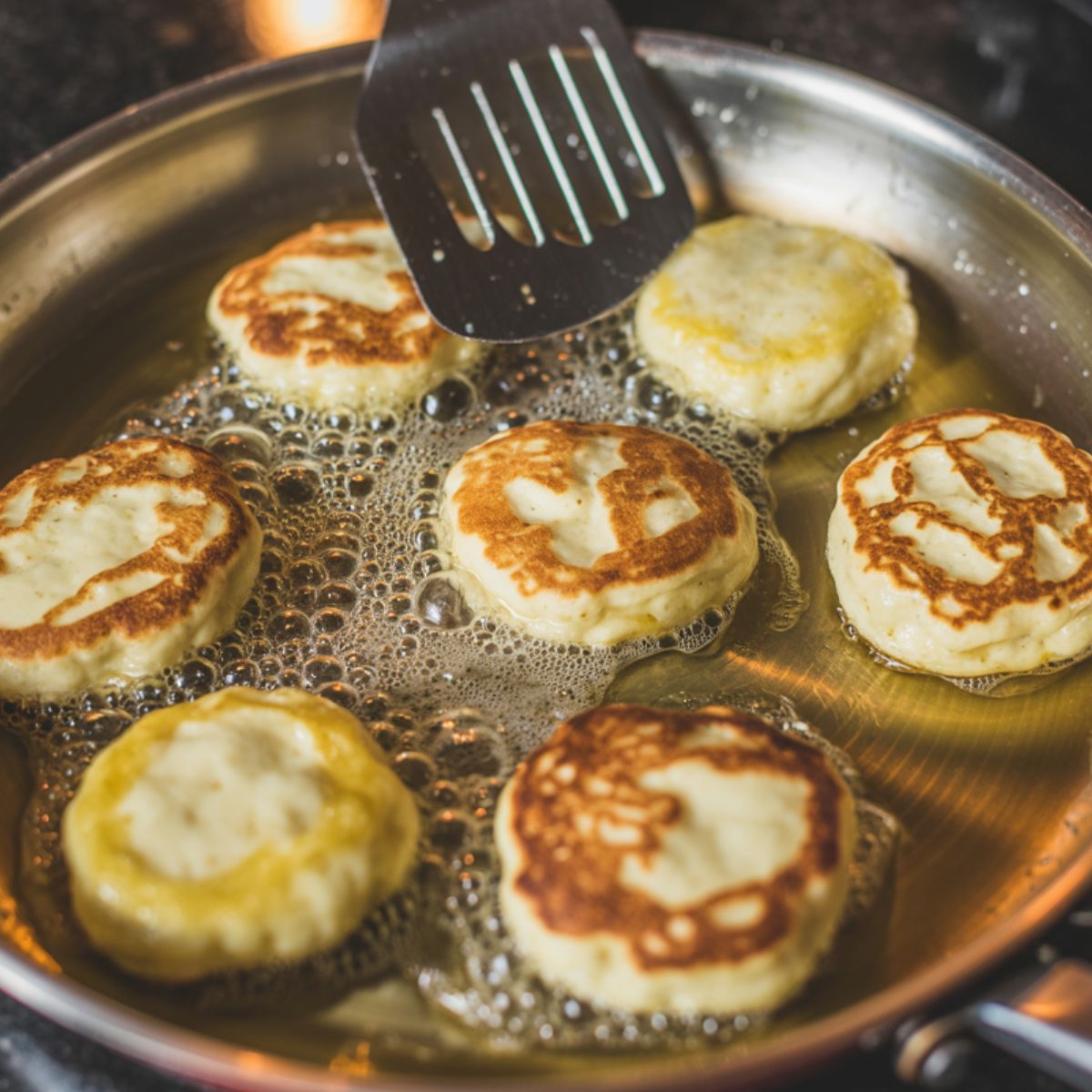  Potato cheese pancakes frying in a skillet, with crisp edges forming.
