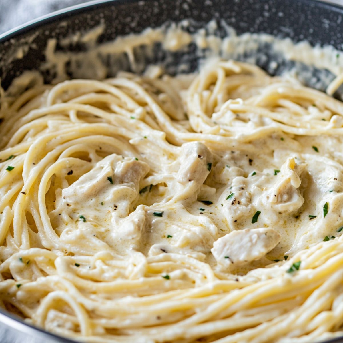 Pasta, chicken, and creamy sauce being mixed before baking.