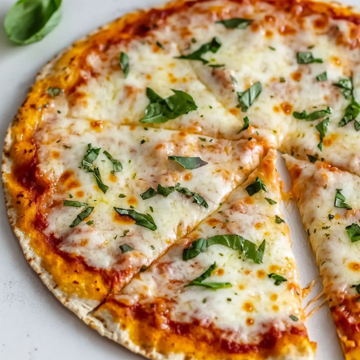 Homemade air fryer tortilla pizza with melted cheese and toppings on a kitchen counter