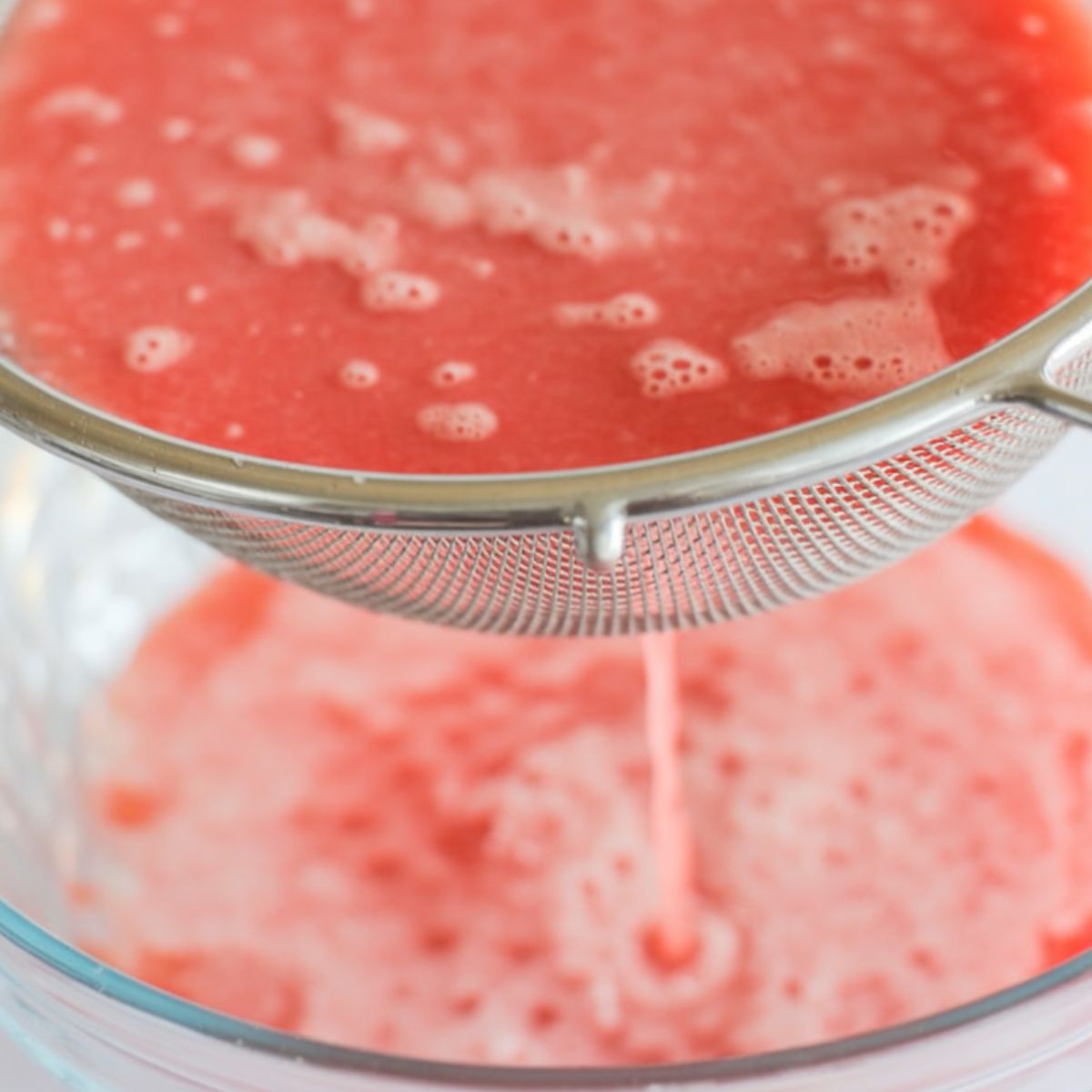 Blended watermelon being poured through a mesh strainer into a bowl
