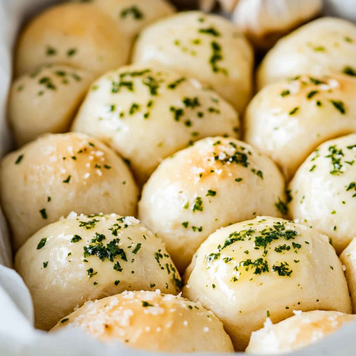 Brushing garlic butter over risen garlic bread rolls before baking