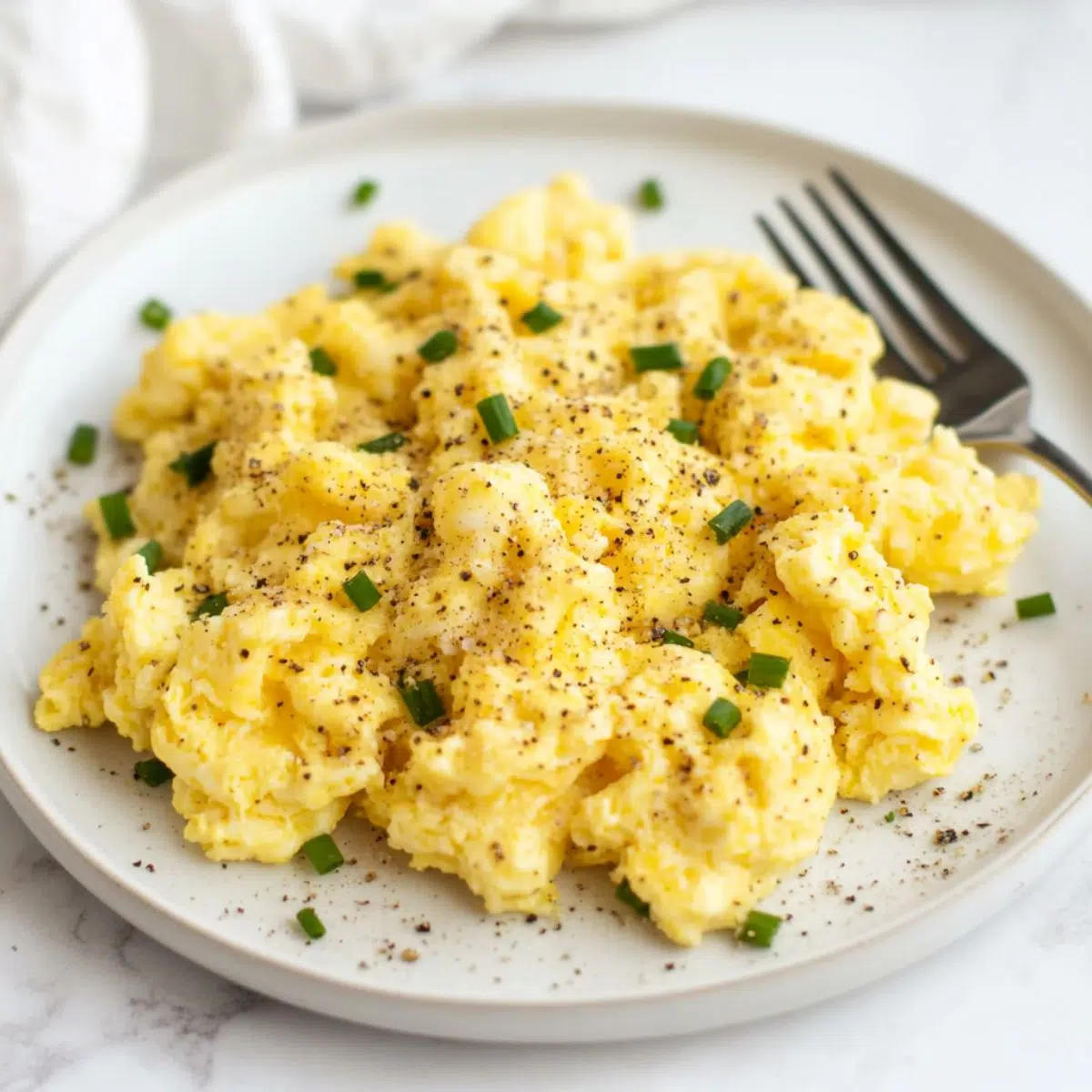Fluffy homemade scrambled eggs recipe served on a plate with pepper and chives.