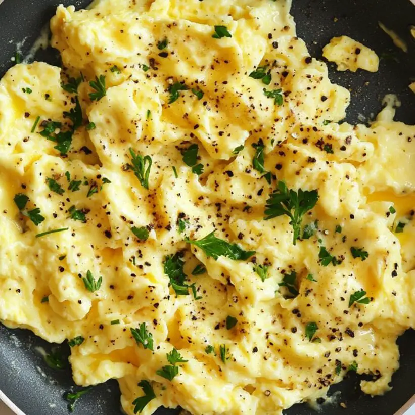 Finished scrambled eggs being garnished with herbs and pepper.