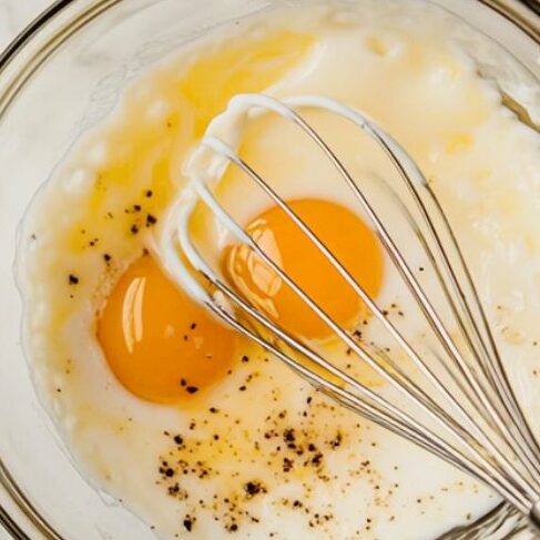  Whisking eggs, milk, and salt in a glass bowl.