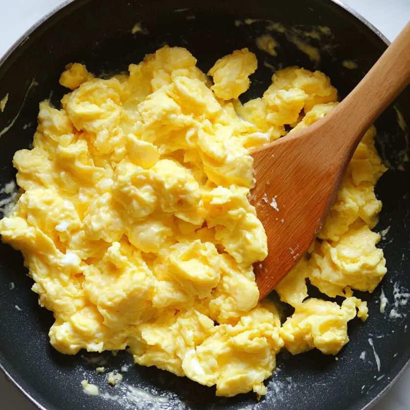 Stirring scrambled eggs gently in a pan with a spatula.