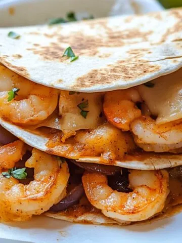 Golden shrimp quesadillas on a plate with melted cheese and sides on a white counter.