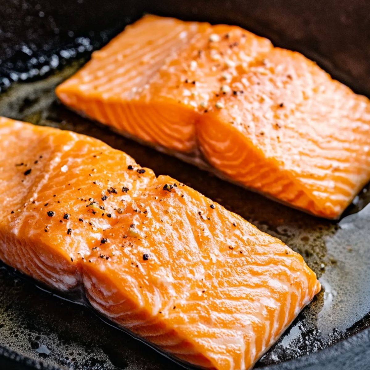 Salmon fillets sizzling skin-side down in a cast iron skillet