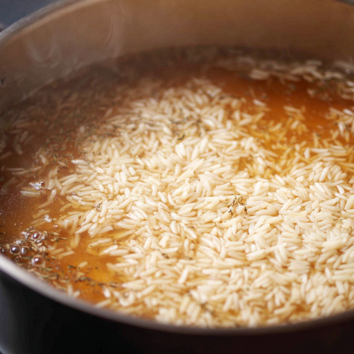 Jasmine rice simmering in a pot of broth on a stovetop