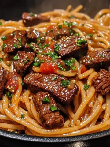 A Skillet of sweet and spicy garlic steak pasta with steak chunks and creamy sauce
