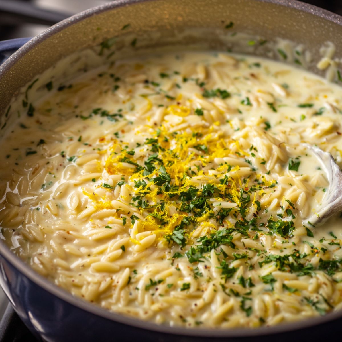 Orzo pasta being mixed into the lemon cream sauce with herbs