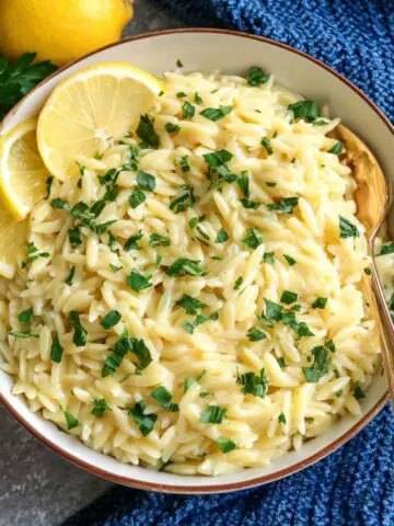Overhead view of creamy lemon orzo pasta with fresh herbs on a white counter