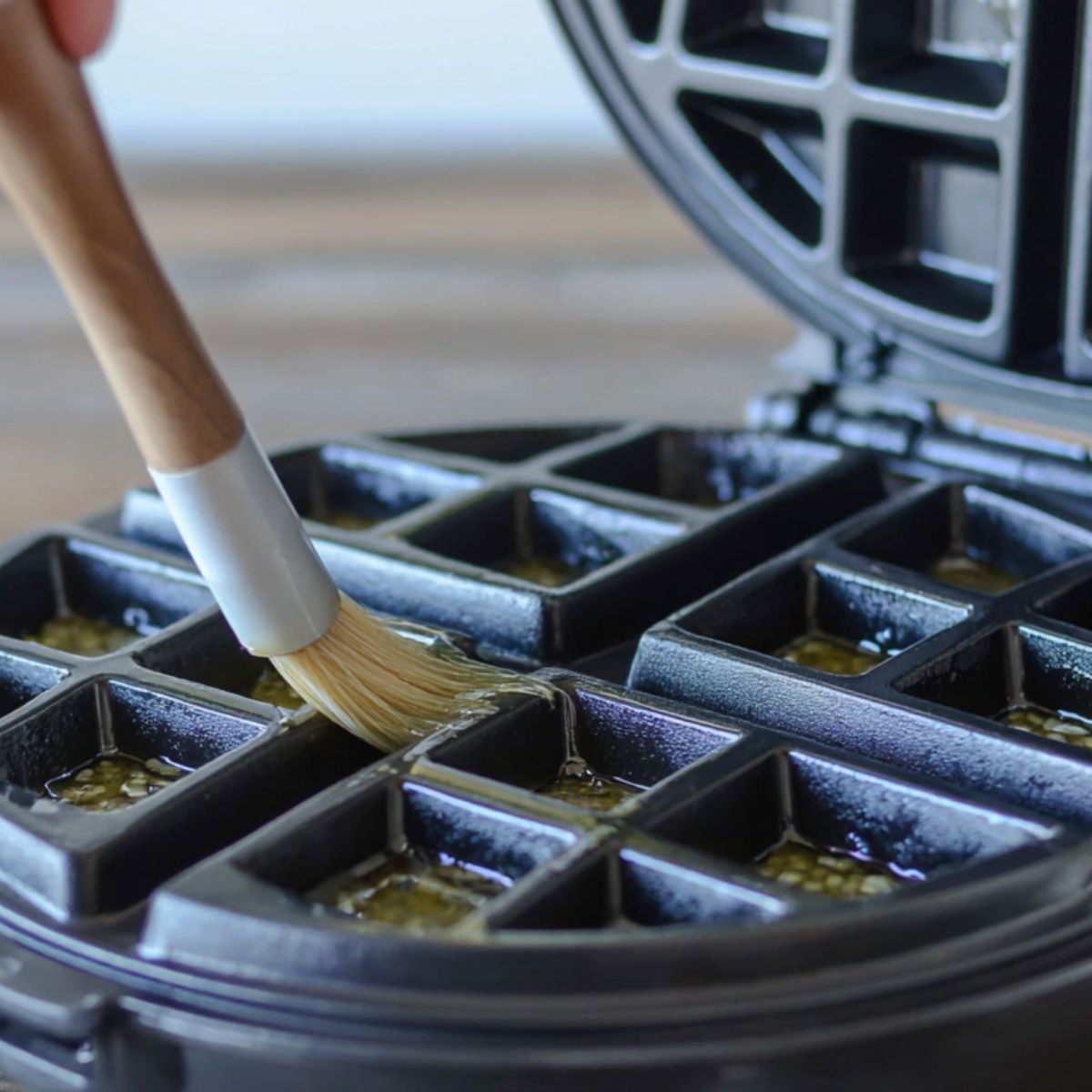  Waffle maker being greased with butter before cooking.