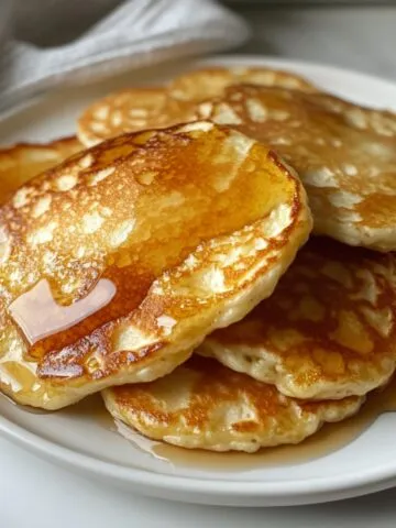 A stack of flourless cottage cheese pancakes with maple syrup, casually plated on a white counter.