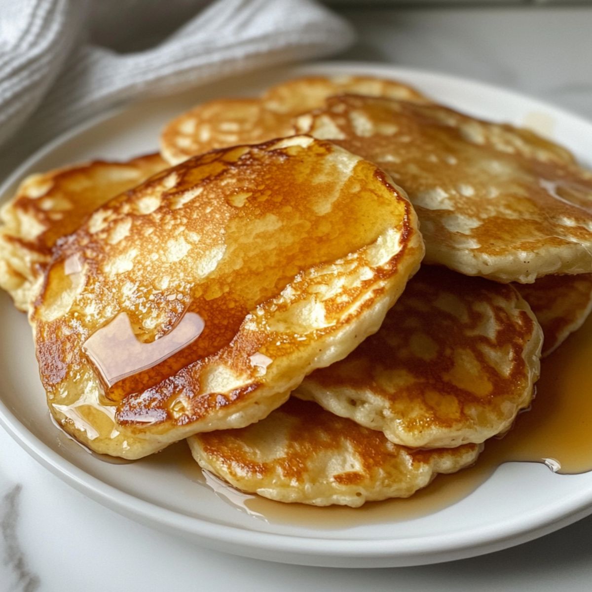 A stack of flourless cottage cheese pancakes with maple syrup, casually plated on a white counter.