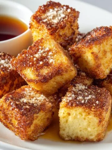 Overhead view of cinnamon french toast bites stacked on a plate with maple syrup on a white kitchen counter