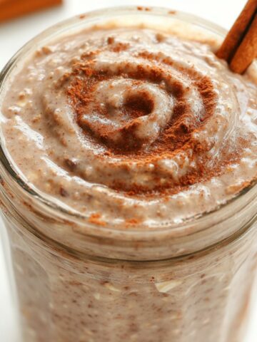 homemade jar of cinnamon roll overnight oats topped with cinnamon drizzle, sitting on a white kitchen counter