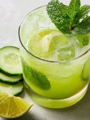 Glass of cucumber lime agua fresca with fresh ingredients on a white counter
