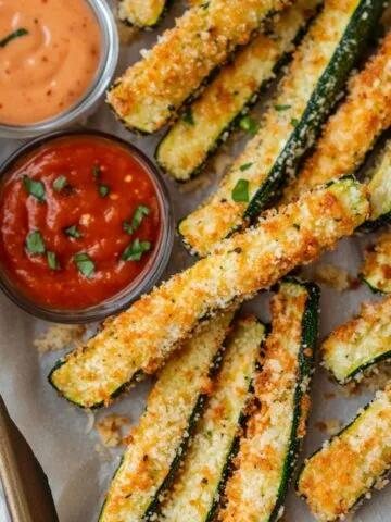 Crispy homemade parmesan zucchini fries served with dipping sauces on a kitchen counter.