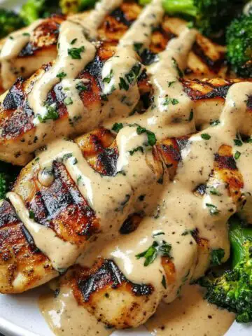 Grilled chicken and broccoli with creamy garlic sauce served on a plate.