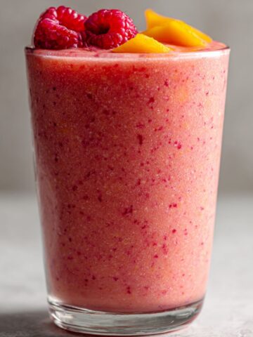 Homemade Raspberry Peach Smoothie in a glass with scattered fruit