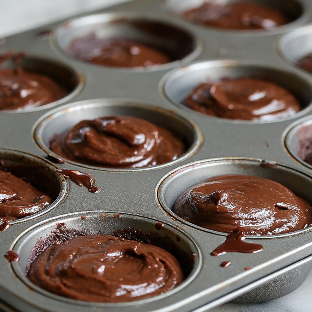 Spoon filling mini muffin tin with brownie batter