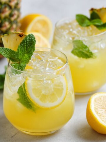 Two glasses of Refreshing homemade pineapple lemonade with lemon and mint on a white kitchen counter