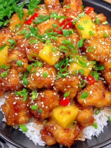 A plate of Sweet Hawaiian Crockpot Chicken over rice with pineapple and bell peppers.