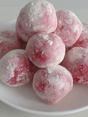 Homemade watermelon mochi balls on a plate, soft pink color with natural imperfections, on a white kitchen counter.