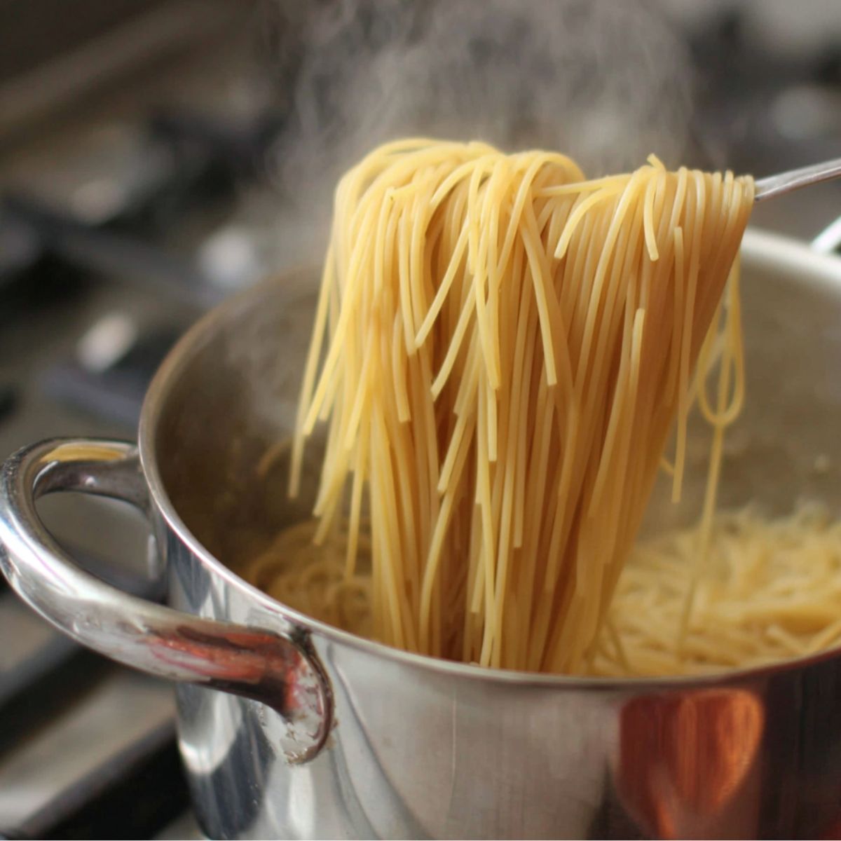 Pasta boiling in a pot with a bowl of reserved water beside it.